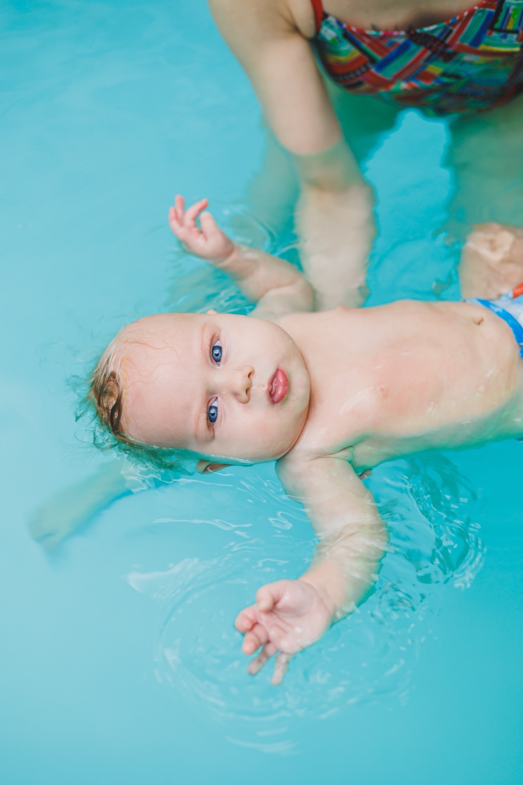 Copil învățând să înoate în piscină, cu un antrenor